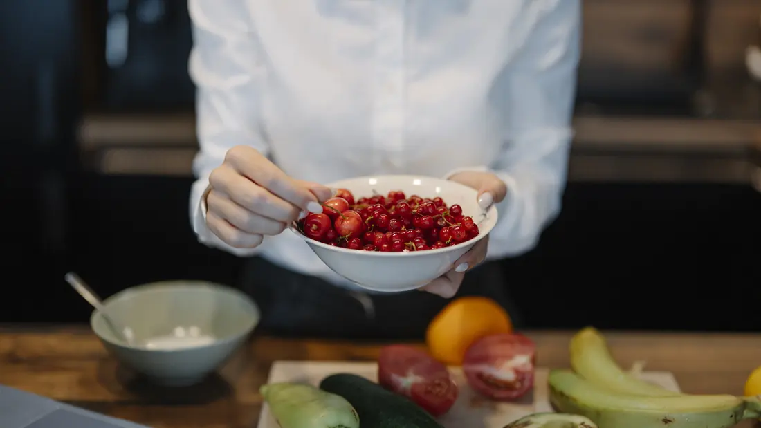 A person holding a bowl of red berries while cooking in a kitchen