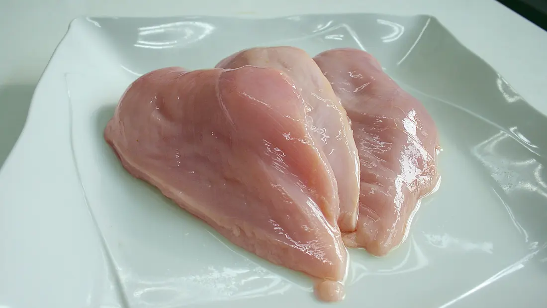 Slices of raw chicken breast laid out on a board