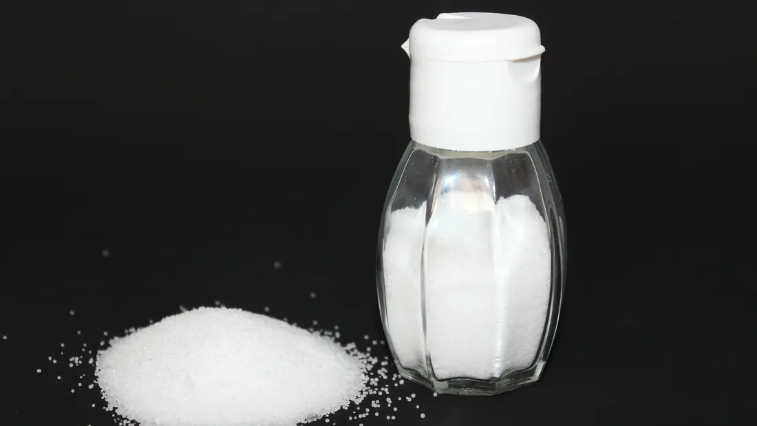 A glass salt shaker beside a spoon of salt